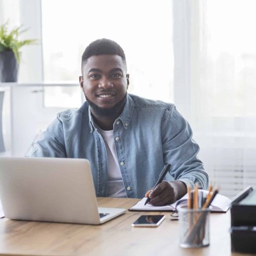 Portrait of smiling black trainee taking notes at new workplace