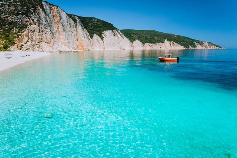 Small red boat on clear blue sea water near to amazing beach on mediterranean island. Summer beach